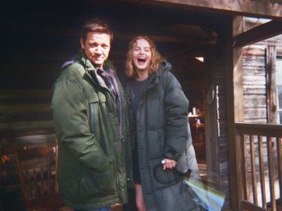 Emma Laird and Jeremy Renner are both wearing big jackets as they are smiling at the camera.